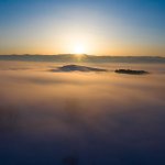 Letecký záber východu slnka nad hmlistou krajinou a horami